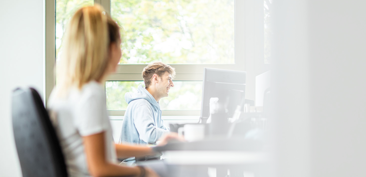 Zwei Mitarbeiter lachend an ihren Arbeitsplätzen